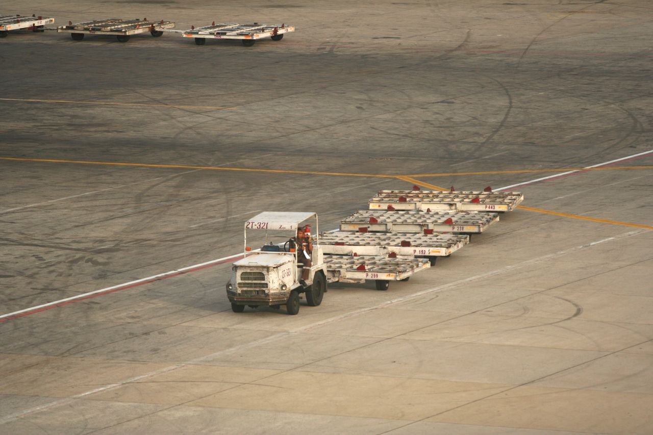 Home Ground crew vehicle transporting baggage carts on airport tarmac, aerial view.
